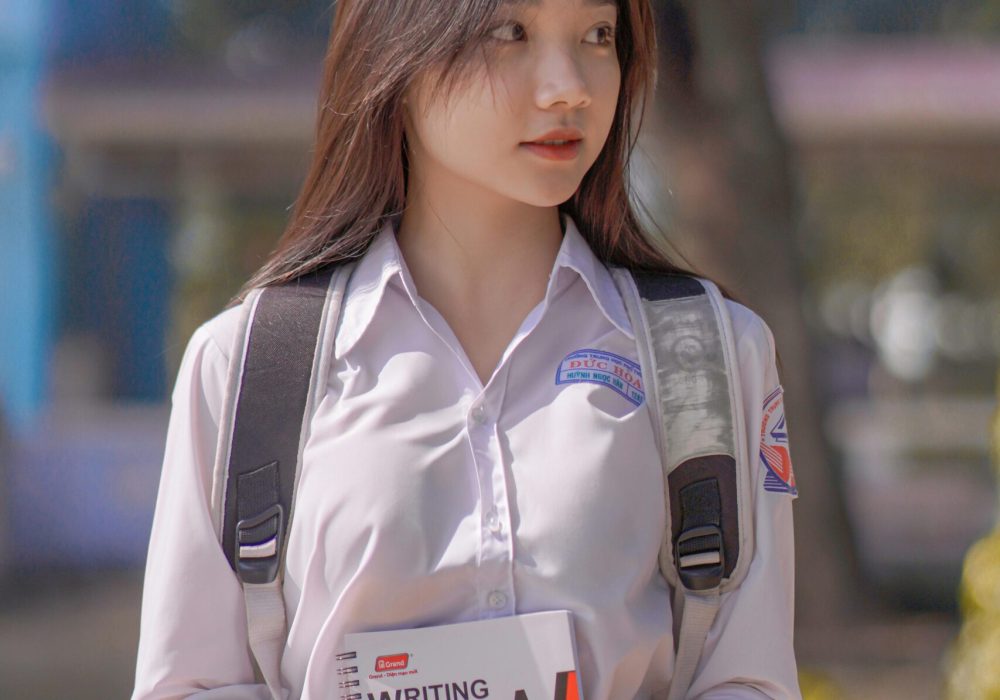 A teenage student in a school uniform holds a notebook outdoors, showcasing youth and education.