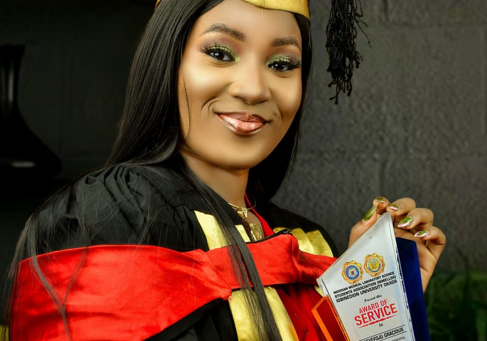 Young woman in a graduation gown holding a service award smiling.
