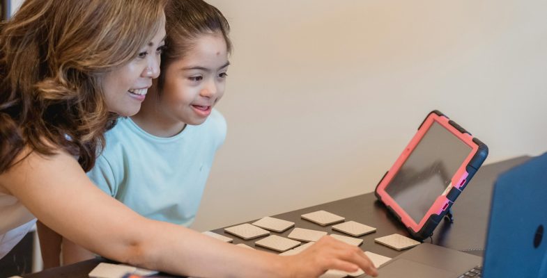 Asian mother and daughter enjoying learning together with a laptop and educational cards indoors.